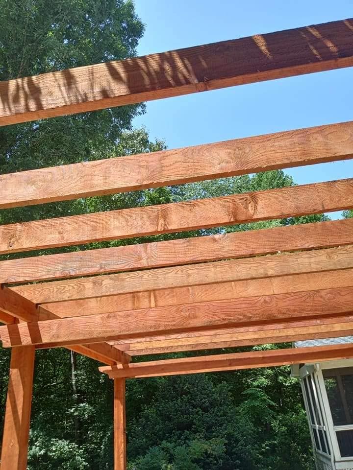 A wooden pergola is being built in the backyard with trees in the background.
