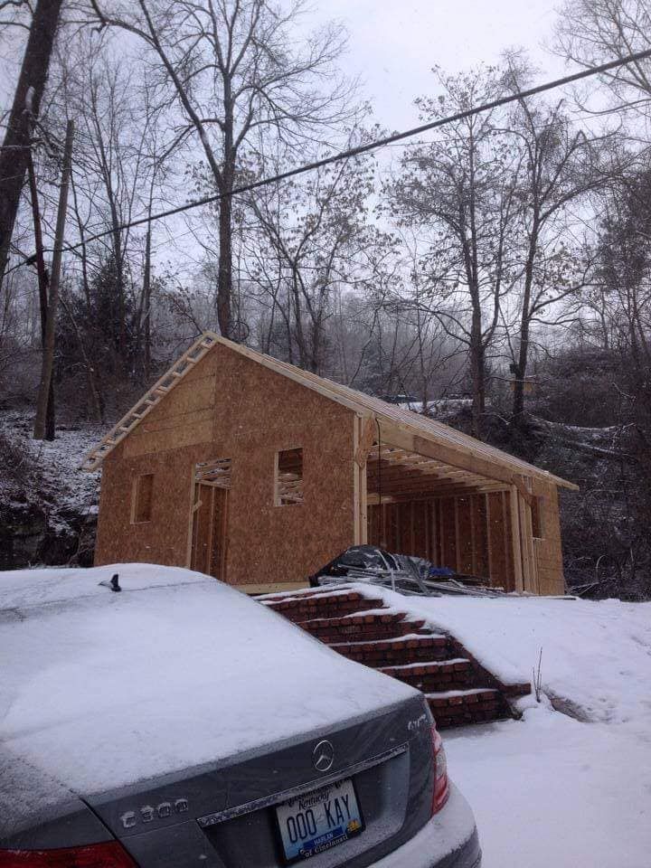 A car is parked in front of a house that is being built in the snow.
