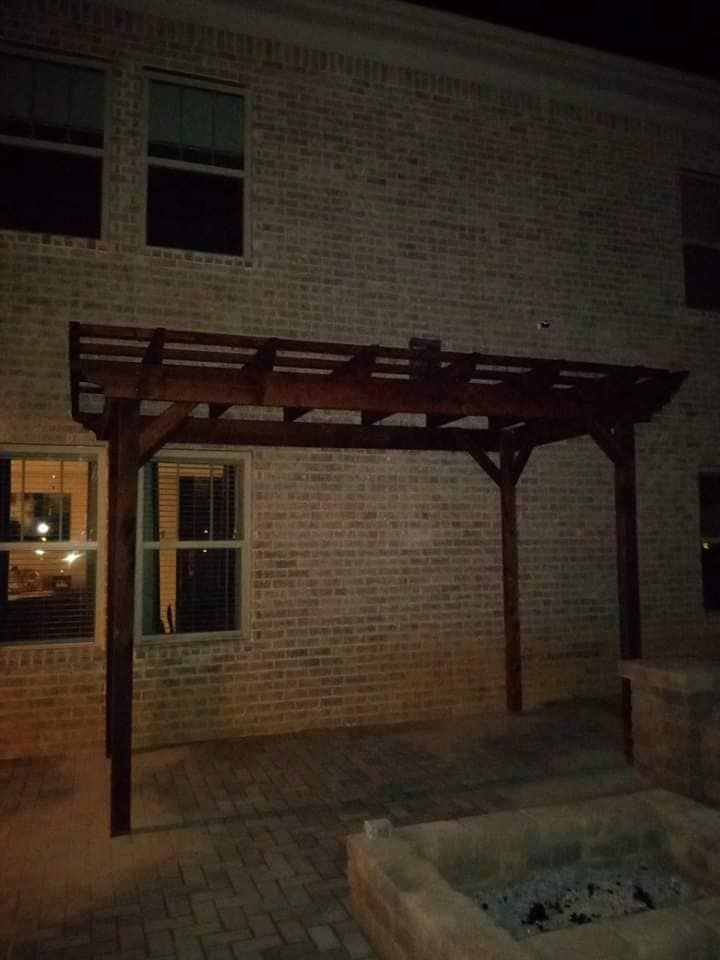 A wooden pergola is sitting in front of a brick building at night.