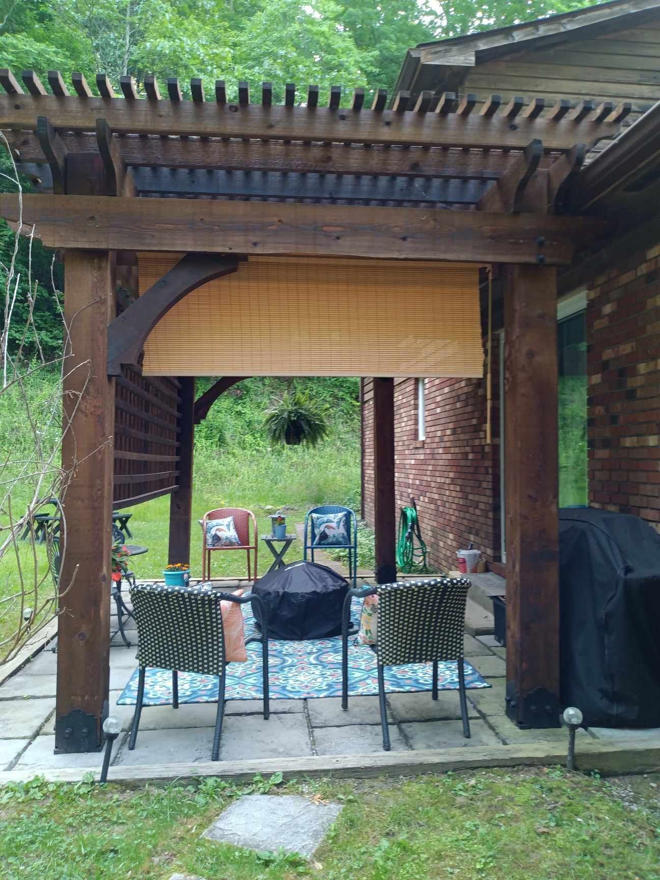 There is a pergola with chairs and a grill underneath it.
