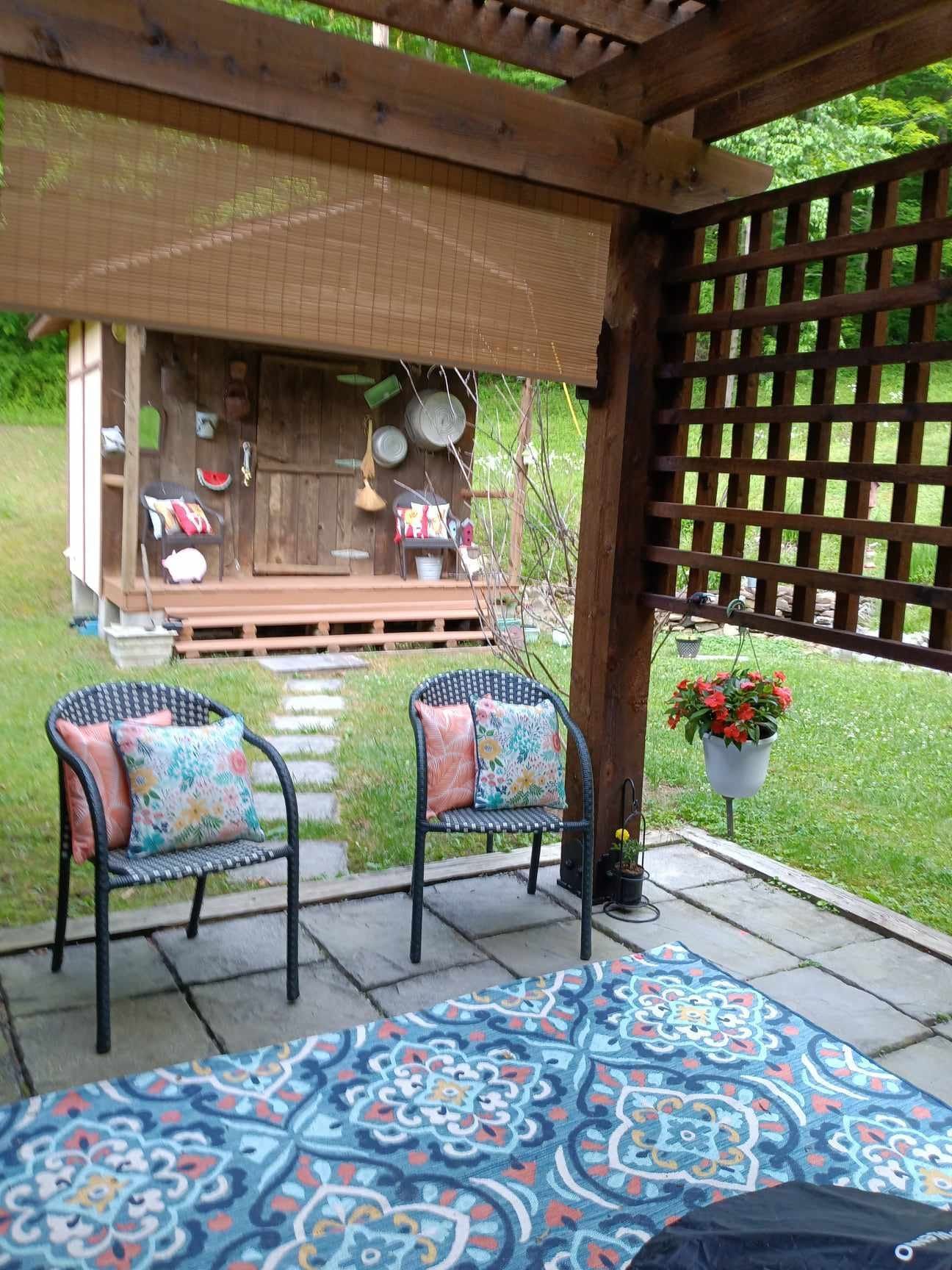 A patio with chairs and a rug under a pergola.