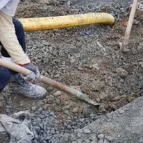A person is kneeling down in the dirt holding a shovel.