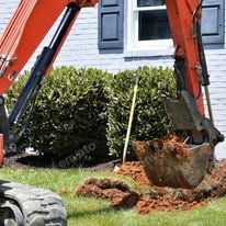 An excavator is digging a hole in the ground in front of a house.