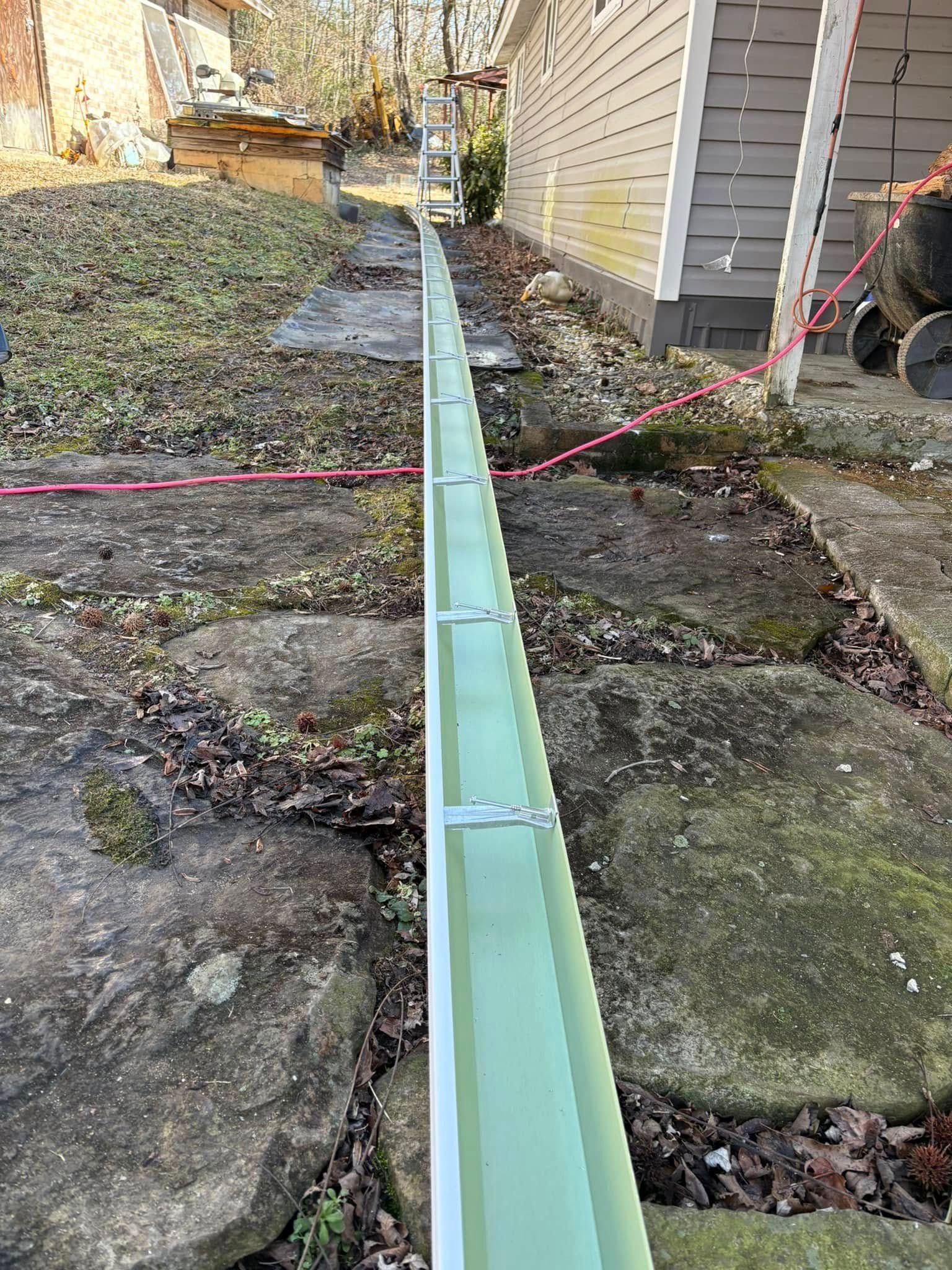 A green gutter is being installed on the side of a house.