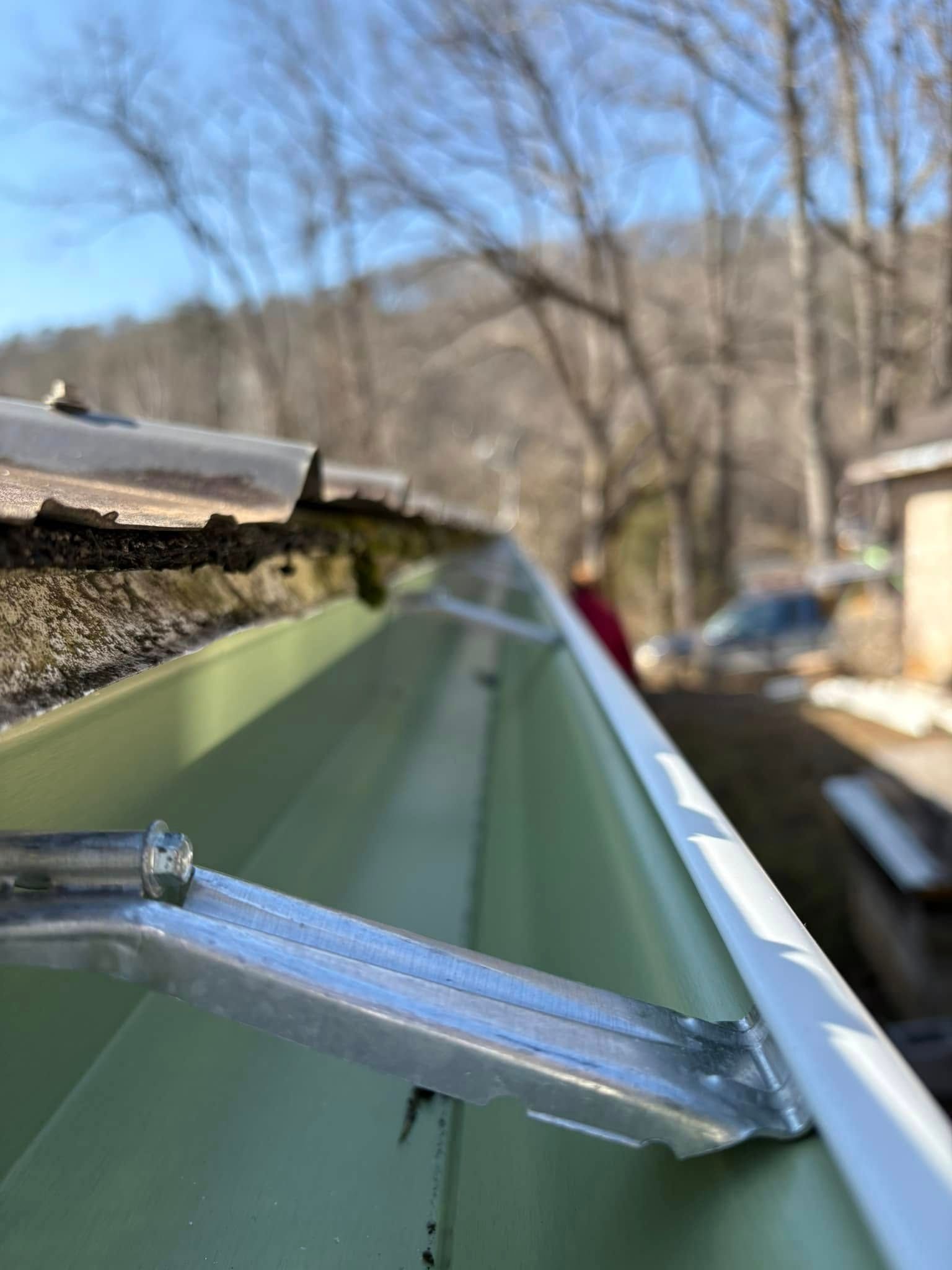 A close up of a green gutter with a metal bracket attached to it.