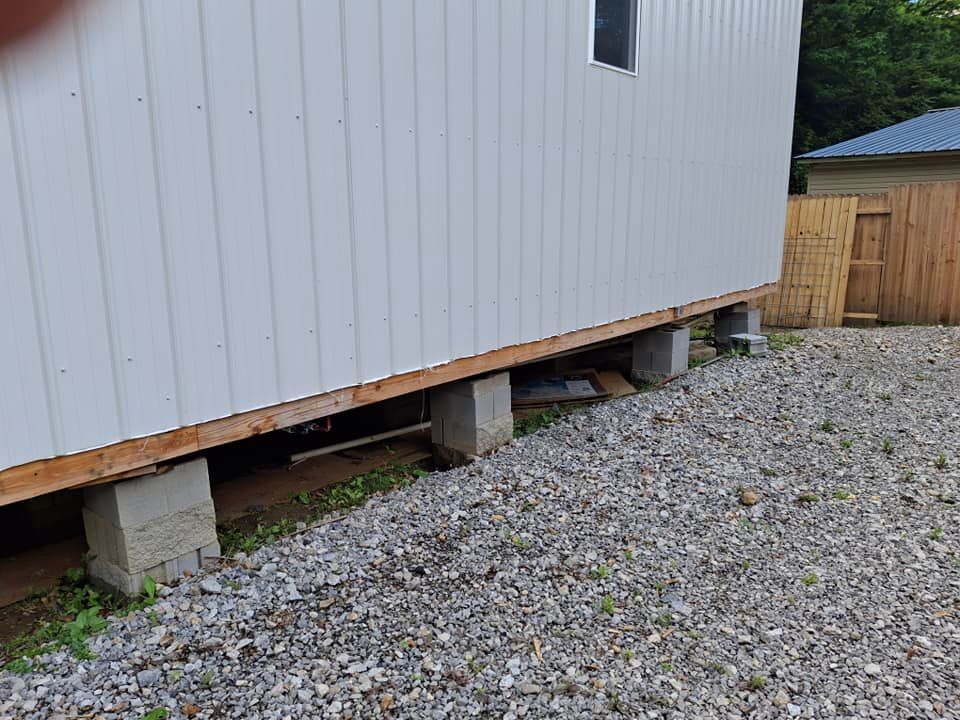 A white building is sitting on concrete blocks in a gravel yard.