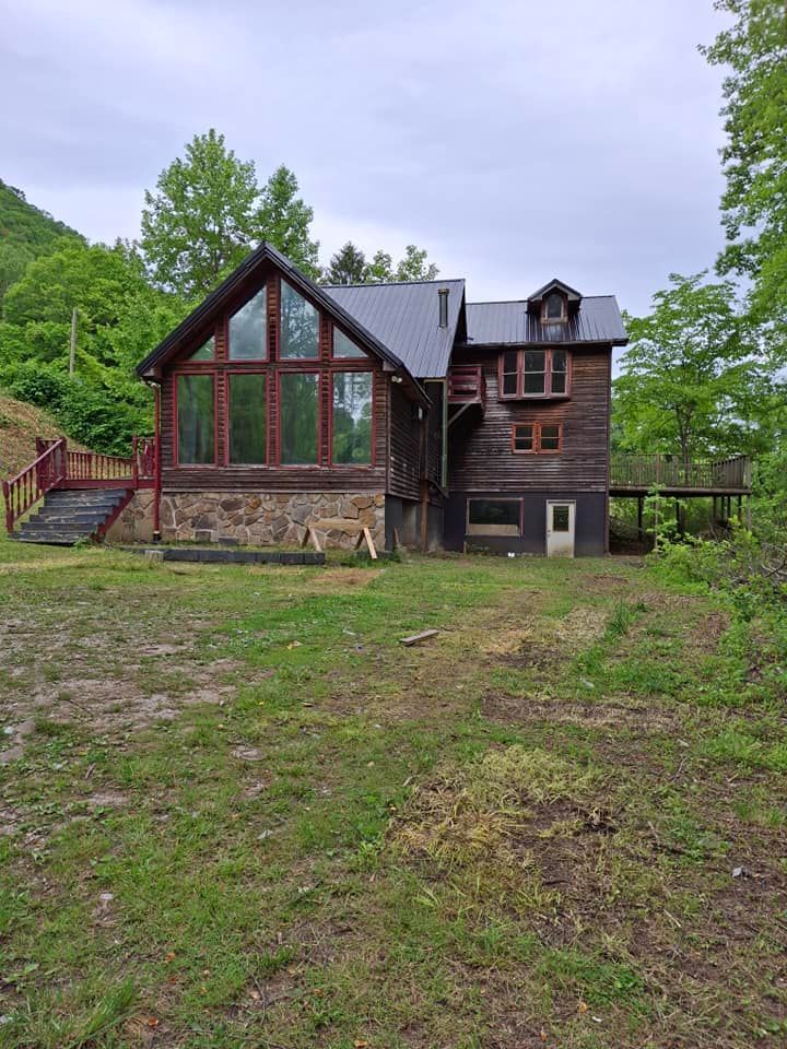 A large wooden house with a lot of windows is sitting in the middle of a grassy field.
