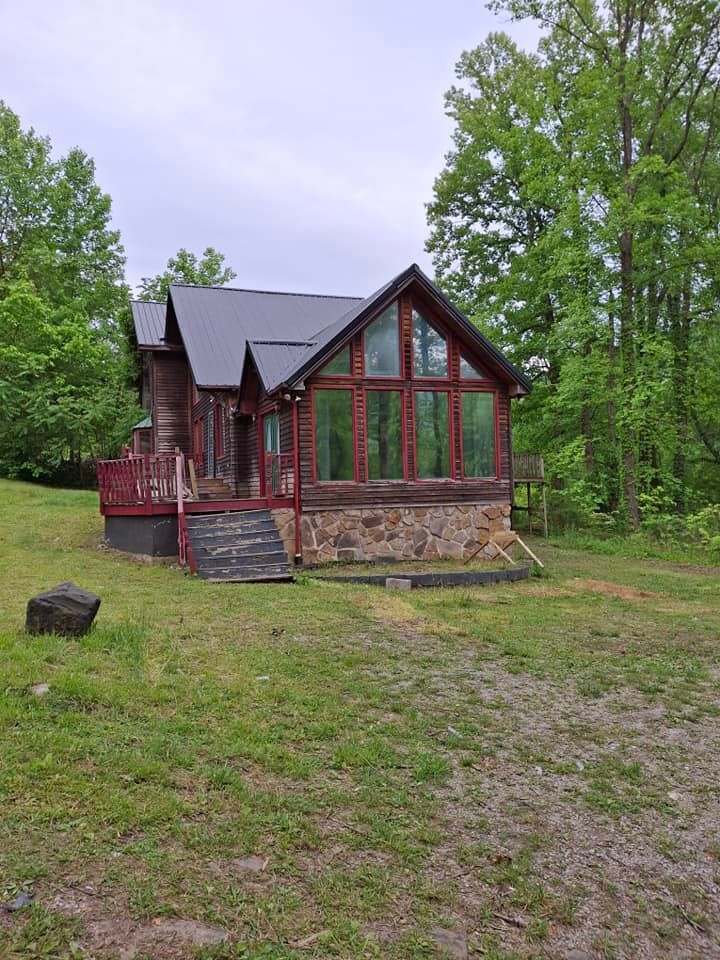 A small log cabin is sitting in the middle of a grassy field surrounded by trees.