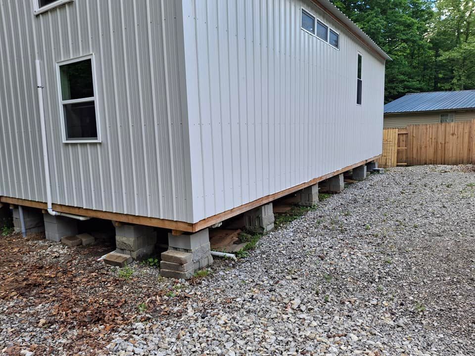 A white house is sitting on top of concrete blocks in a gravel lot.
