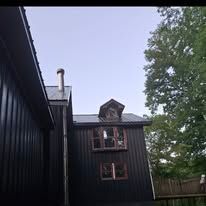 A black house with a chimney on the roof is surrounded by trees.