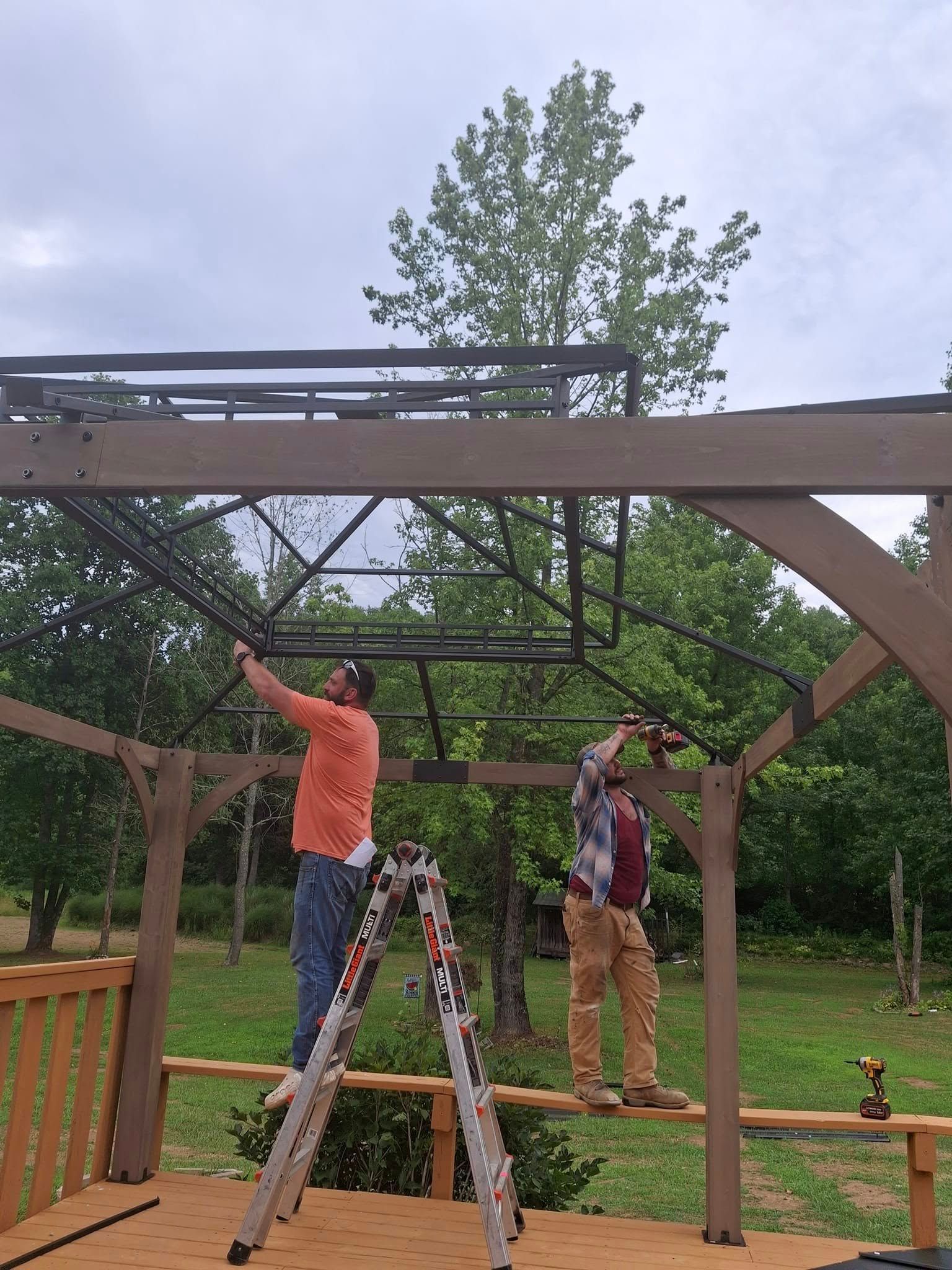 Two men are standing on a ladder working on a wooden structure.