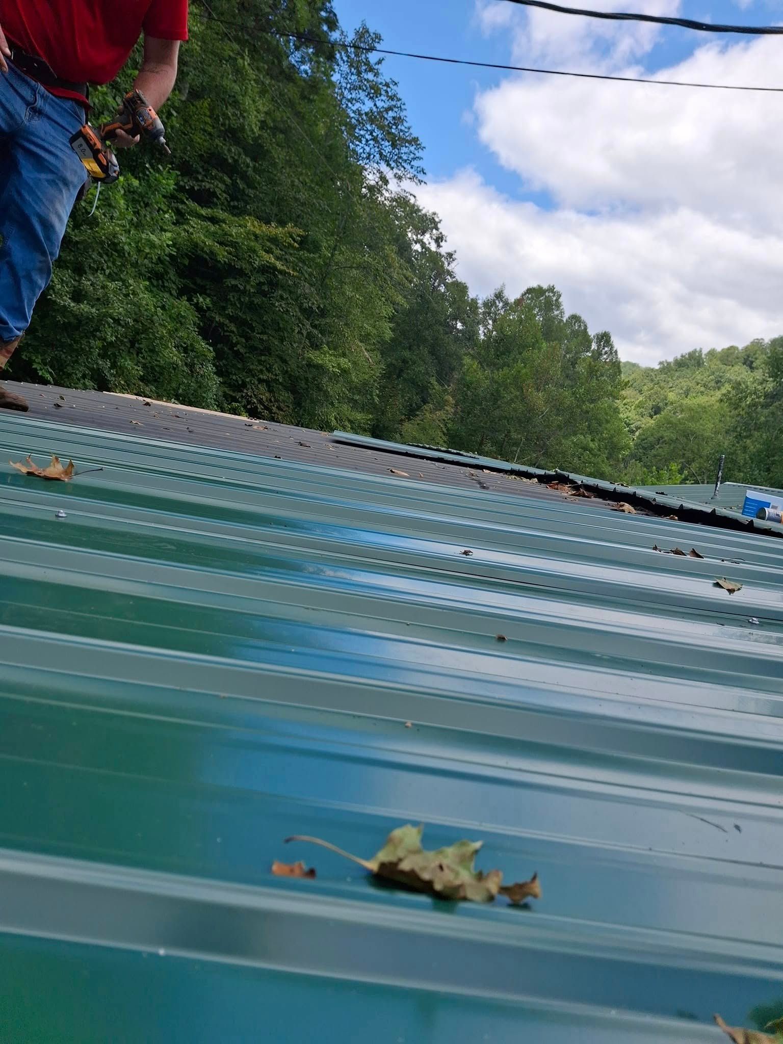 A man is standing on top of a green metal roof.