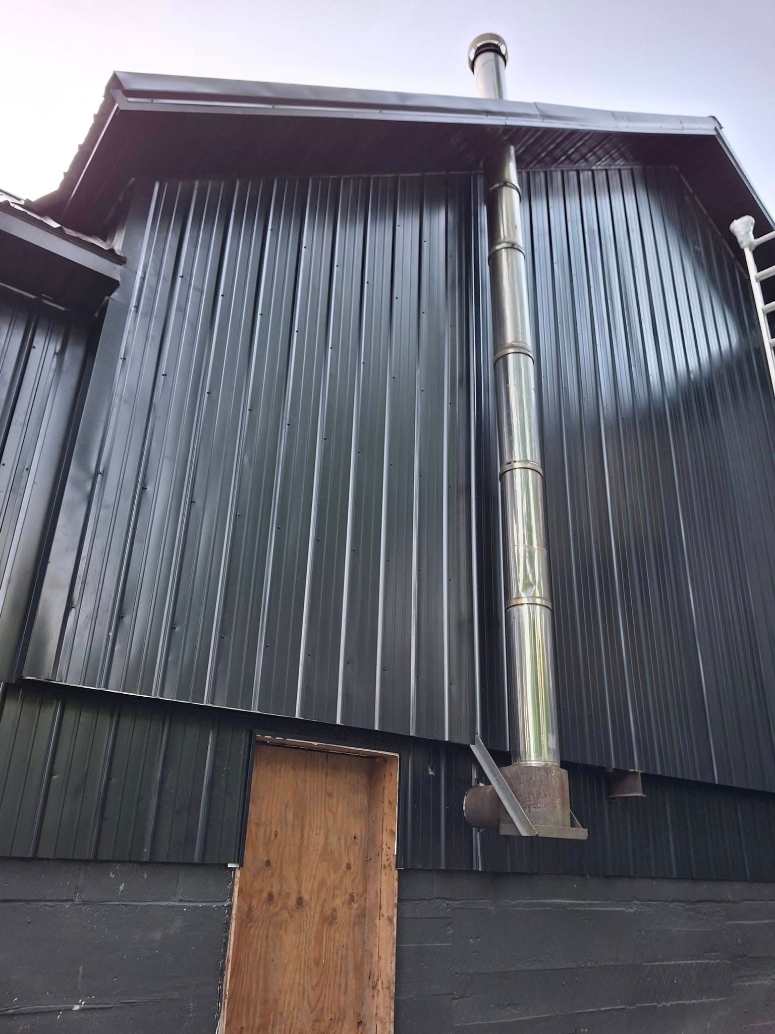 A stainless steel chimney is attached to the side of a building.