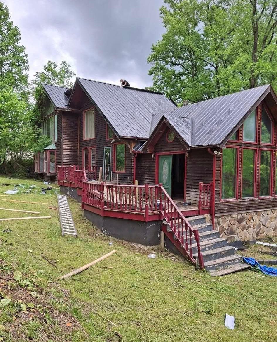A large wooden house with a large deck in the middle of a lush green field.
