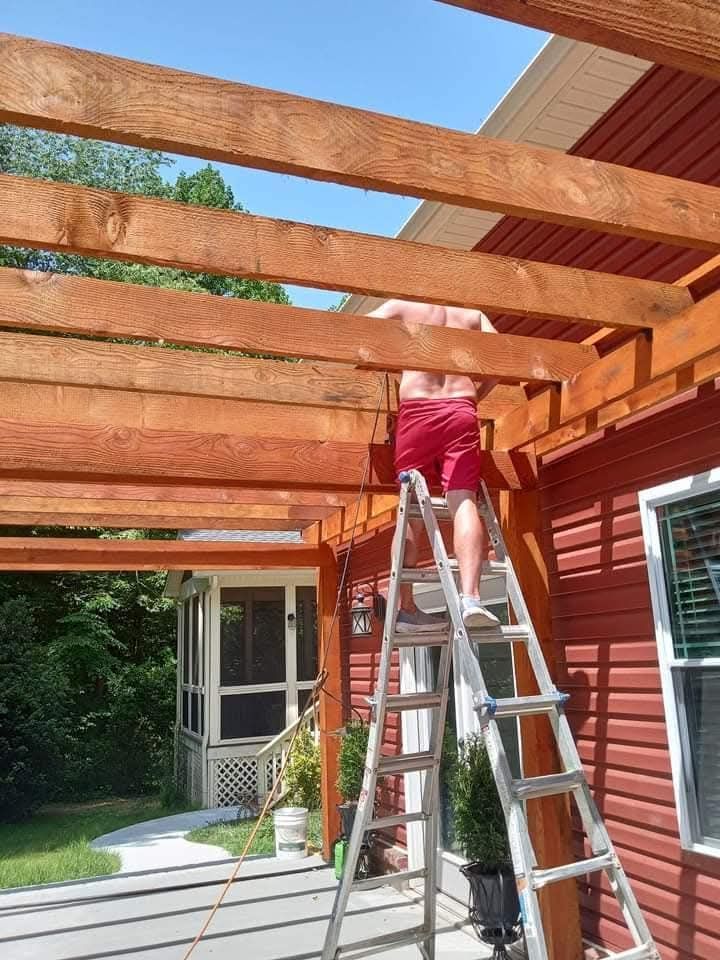A man is standing on a ladder looking up at a wooden structure.