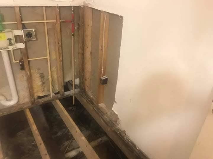 A bathroom with a hole in the wall and a wooden floor.