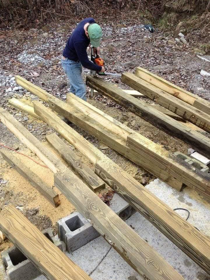 A man is cutting wood with a chainsaw on a pile of wood.