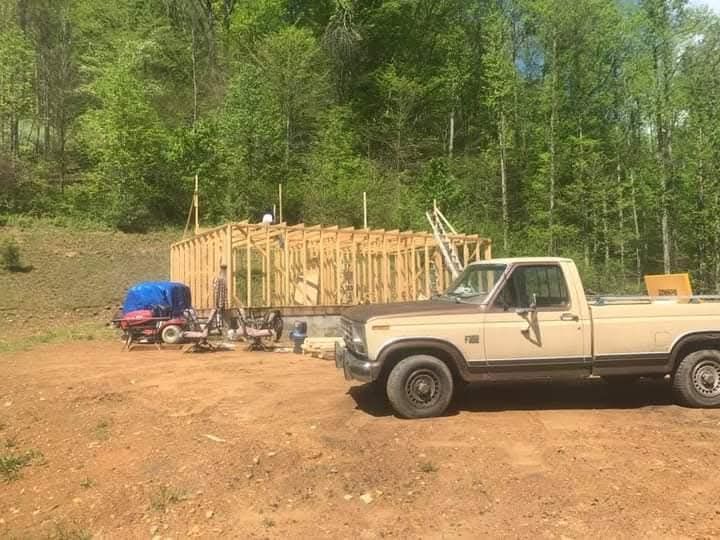 A truck is parked in a dirt lot next to a house under construction.