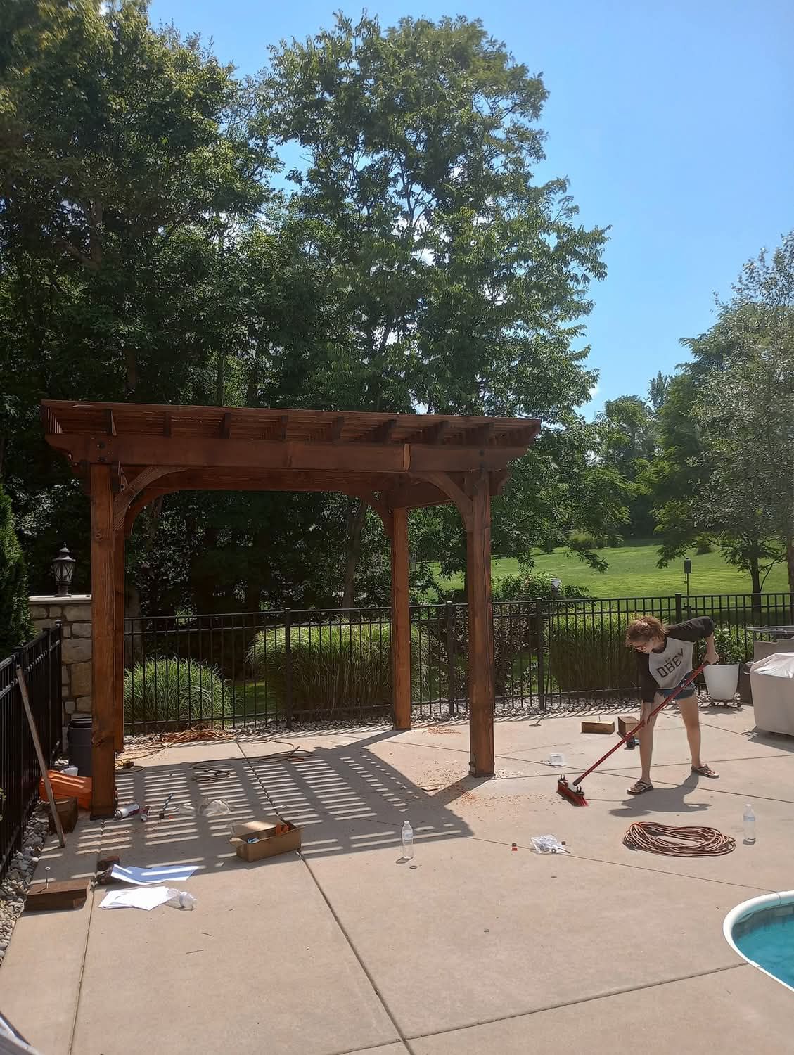 A woman is standing on a patio next to a pool holding a broom.