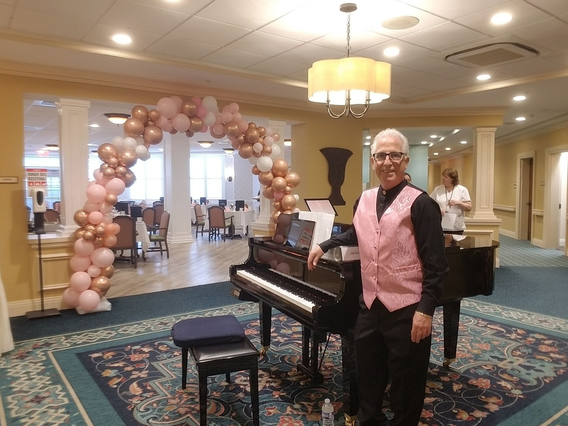 A man in a pink vest is standing in front of a piano.