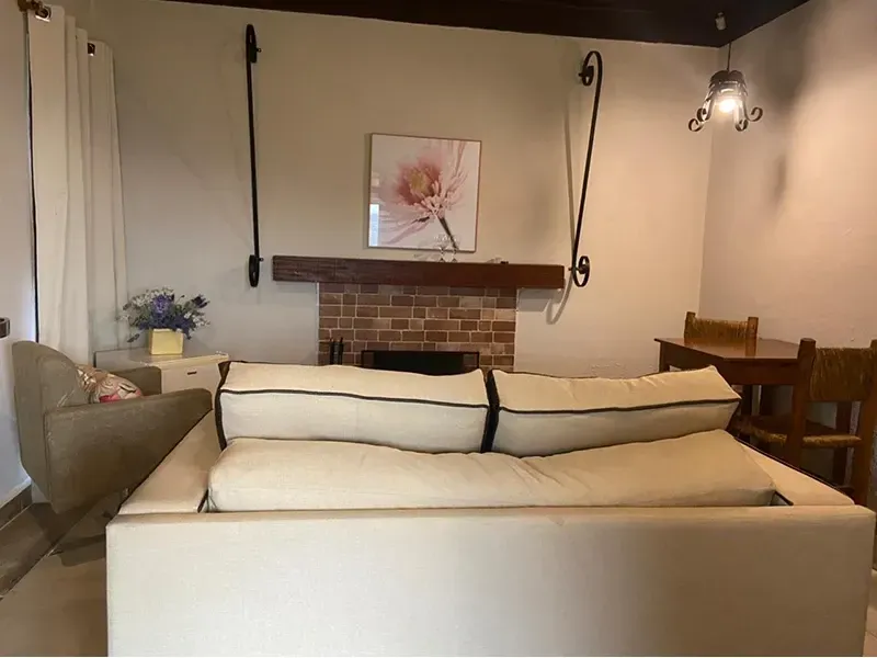 Uma sala de estar com um sofá creme, uma lareira de tijolos com moldura, uma estampa floral e uma pequena mesa de jantar.