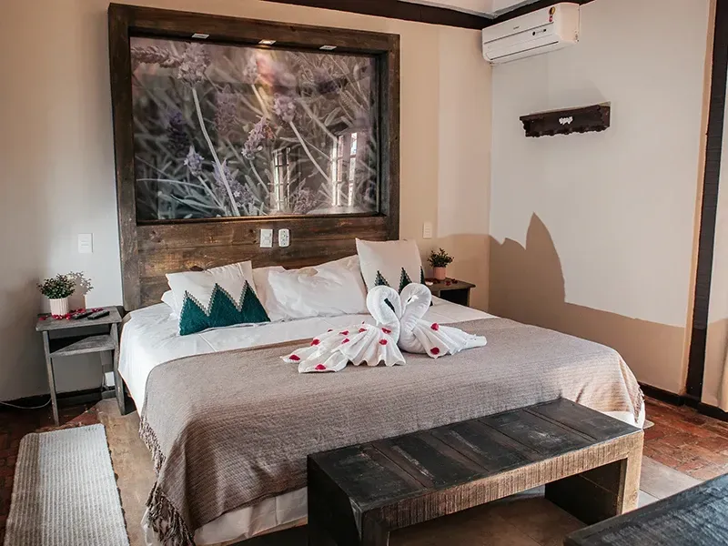 Um quarto de hotel com uma cama grande, adornada com cisnes de toalha decorativos, móveis de madeira e uma cabeceira com tema da natureza.