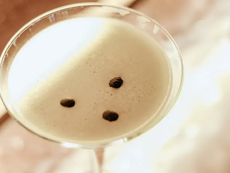 Um espresso martini bege servido em uma taça de coquetel com haste, decorado com três grãos de café sobre a espuma.