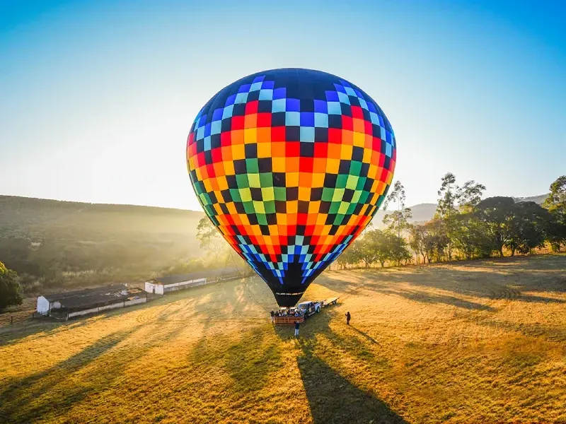 Um balão de ar quente multicolorido, com padrão quadriculado, pousando em um campo dourado ao nascer do sol.