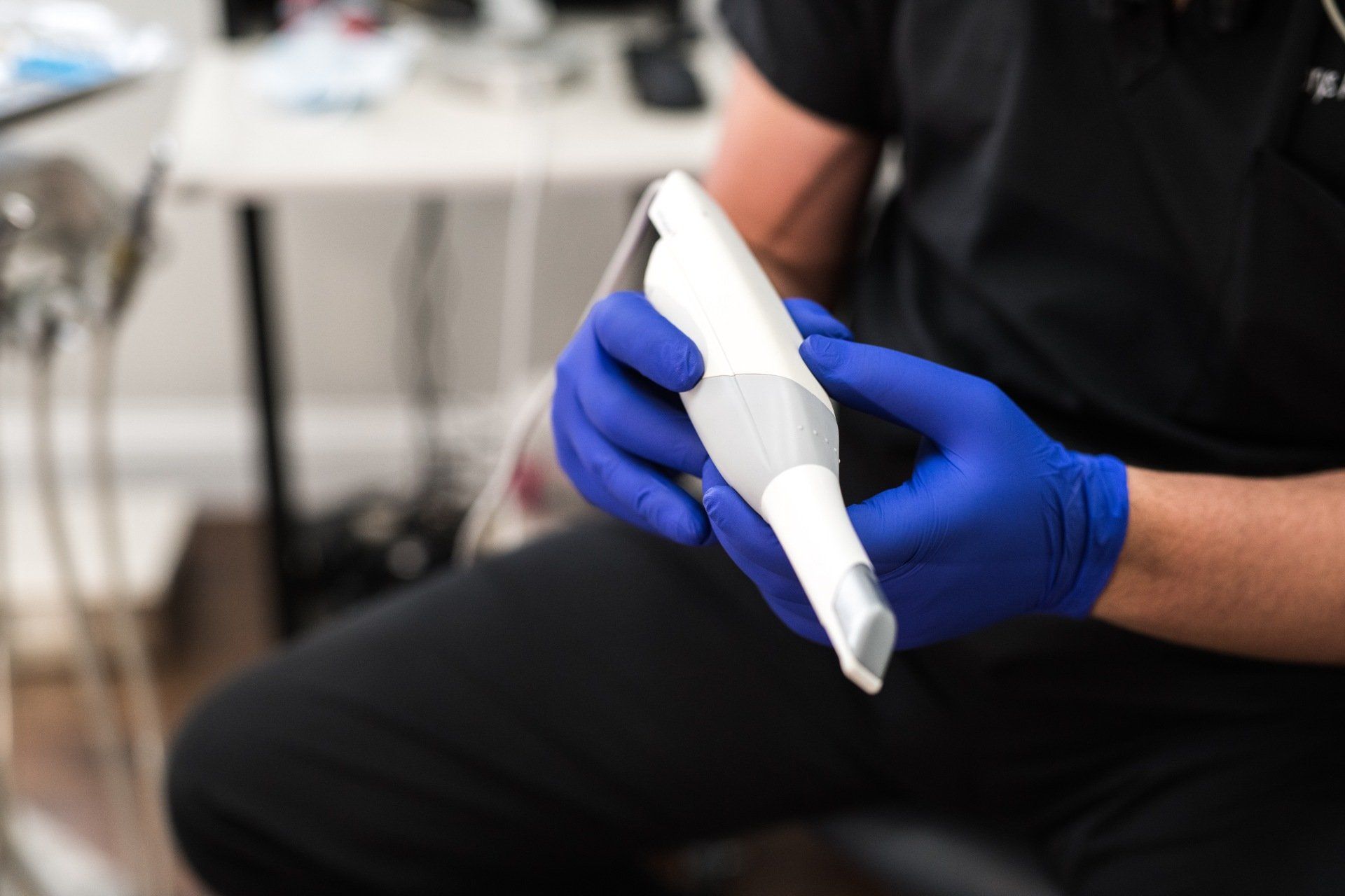 A dentist wearing blue gloves is holding a machine in his hands.