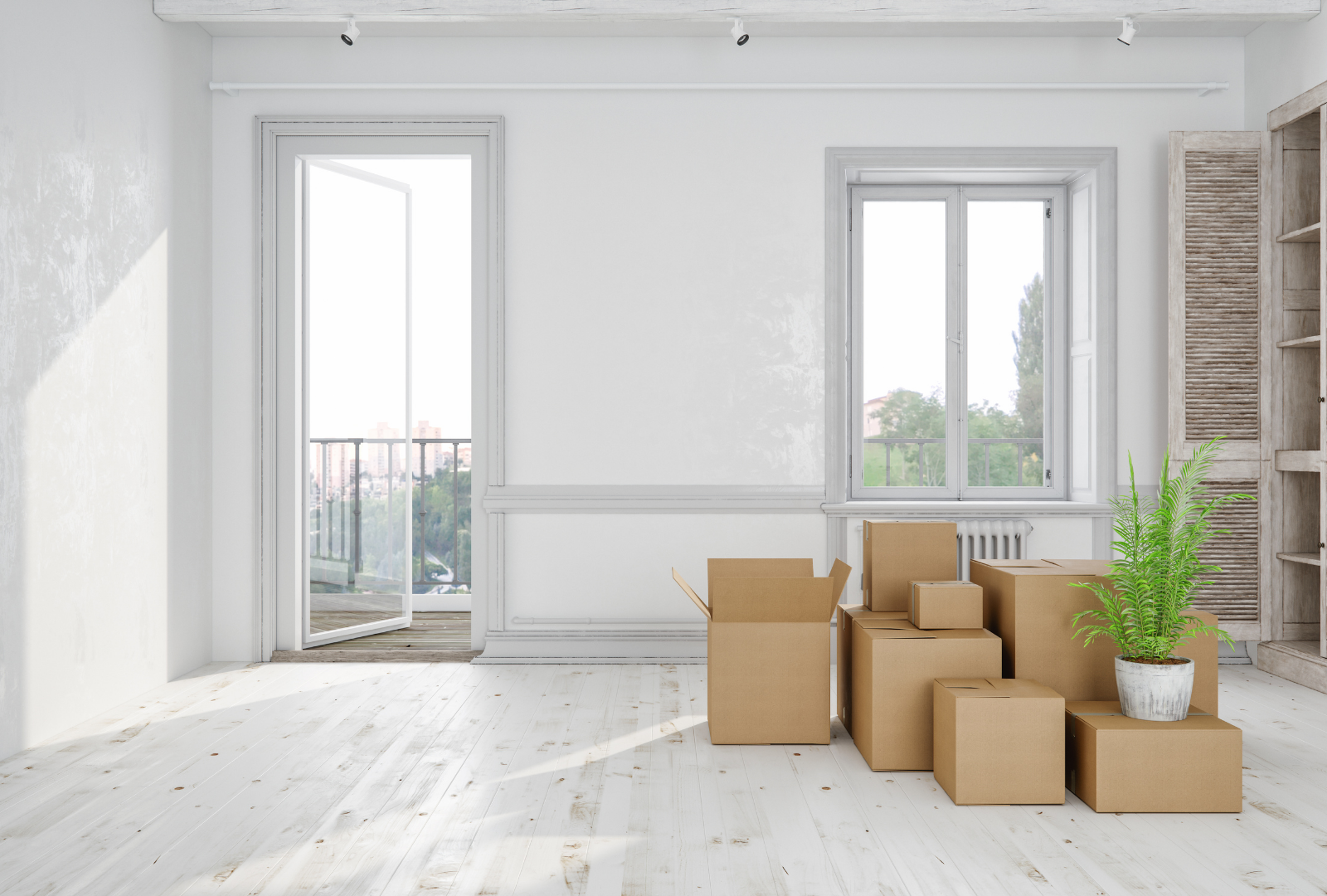 Empty room with cardboard moving boxes and a potted plant by a window and balcony.