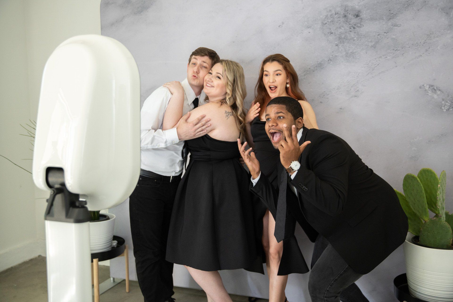Open photobooth with 4 people posing and smiling with a gray background.