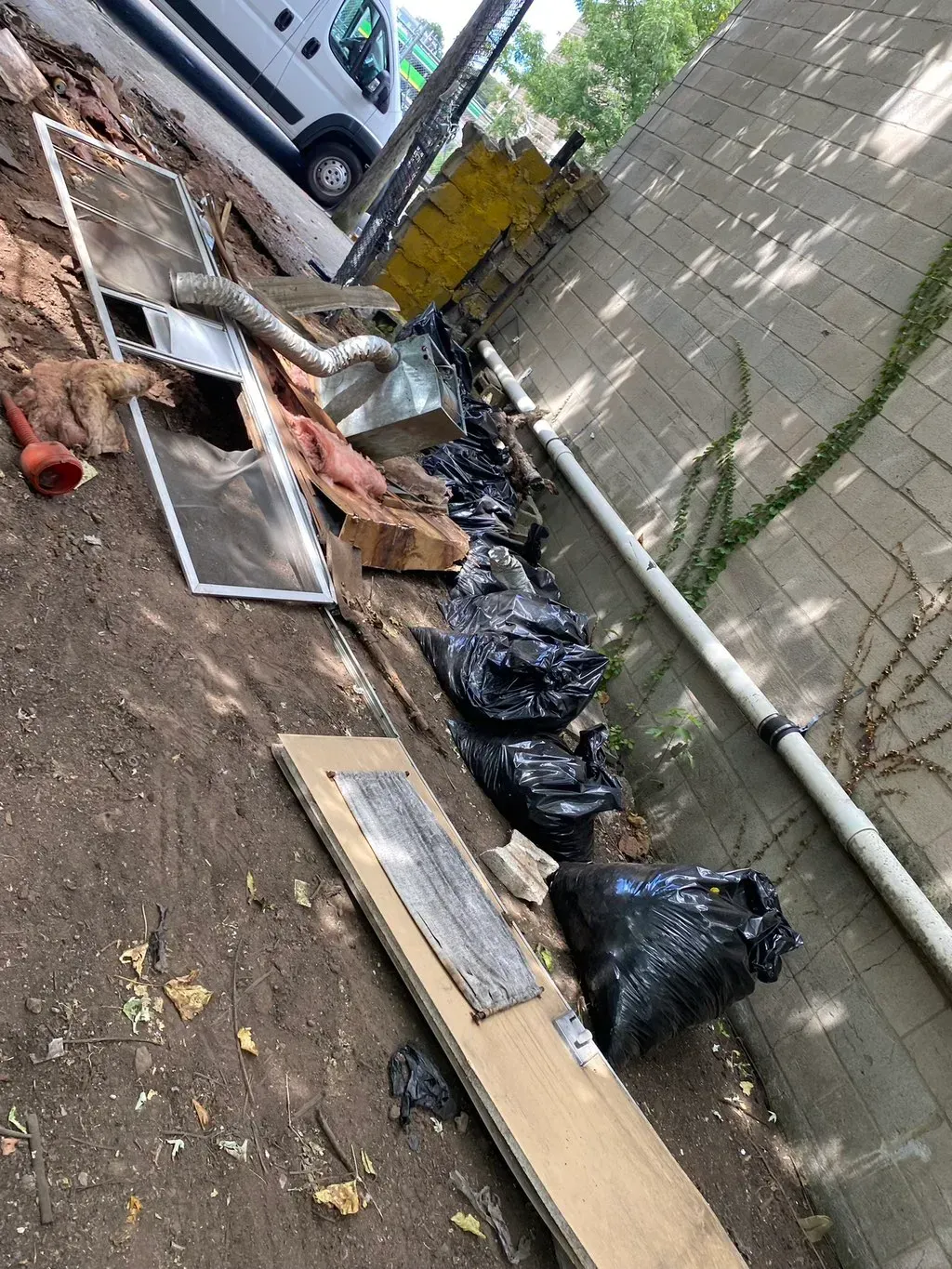 Debris and trash bags on ground next to a concrete wall. A white van is partially visible in the background.