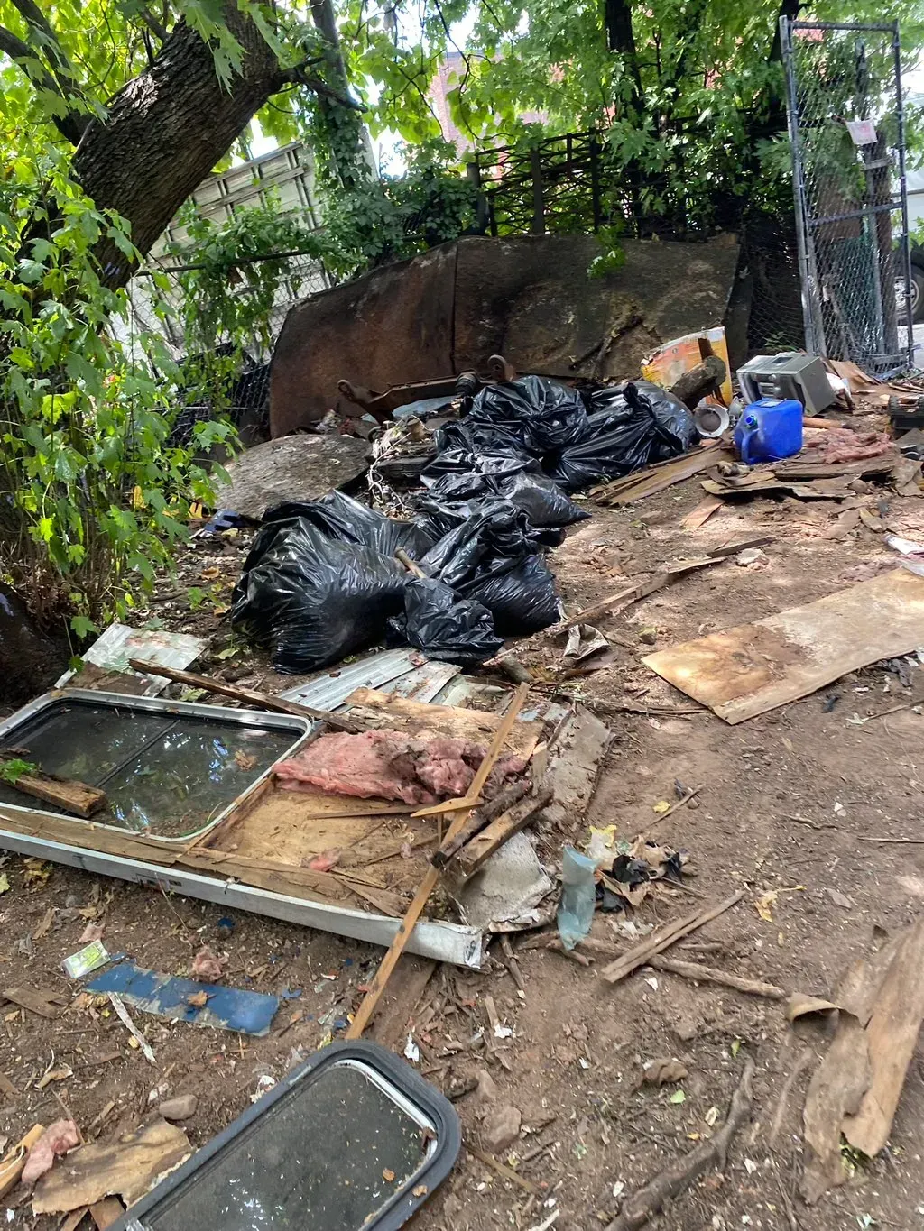 Pile of trash bags, debris, and discarded windows in a dirty, outdoor area.