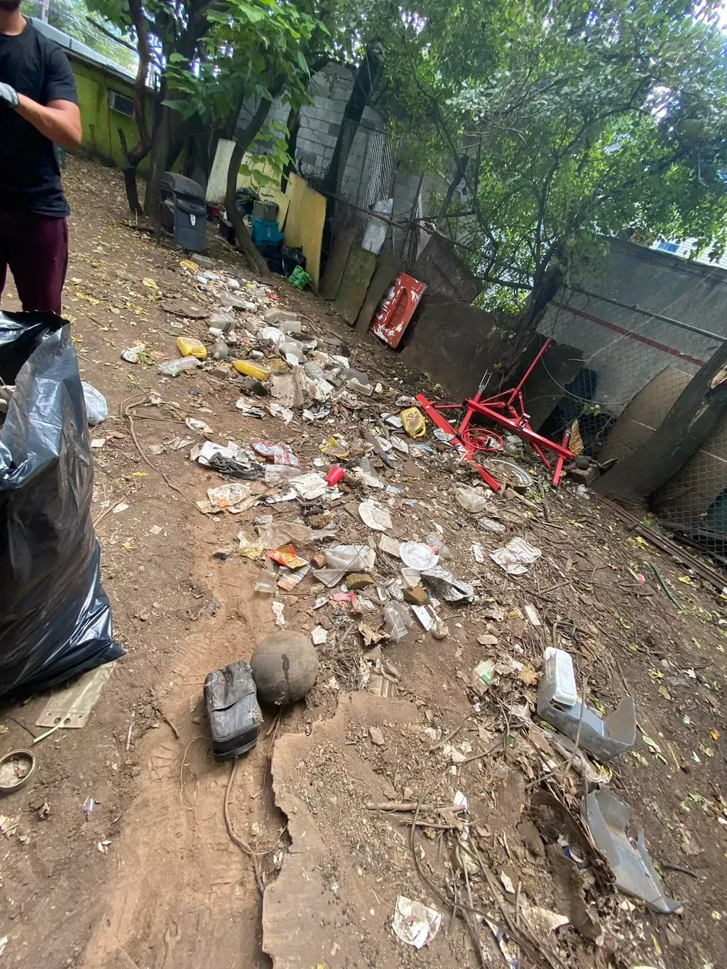 People cleaning up trash along a dirt path; green trees in the background.