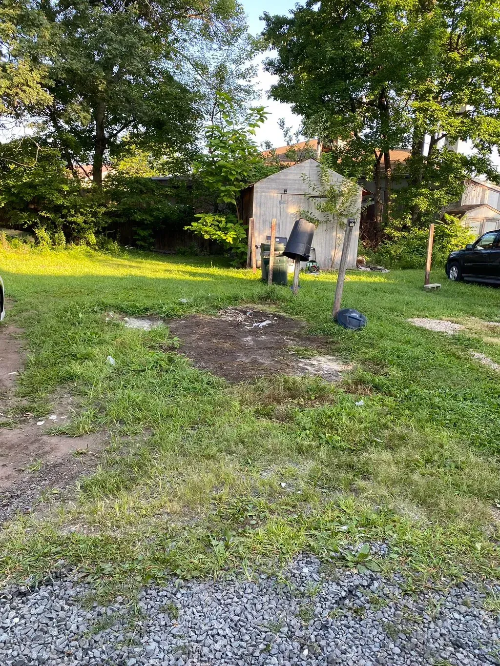 Grassy backyard with a small shed, trees, and a dark patch of dirt.