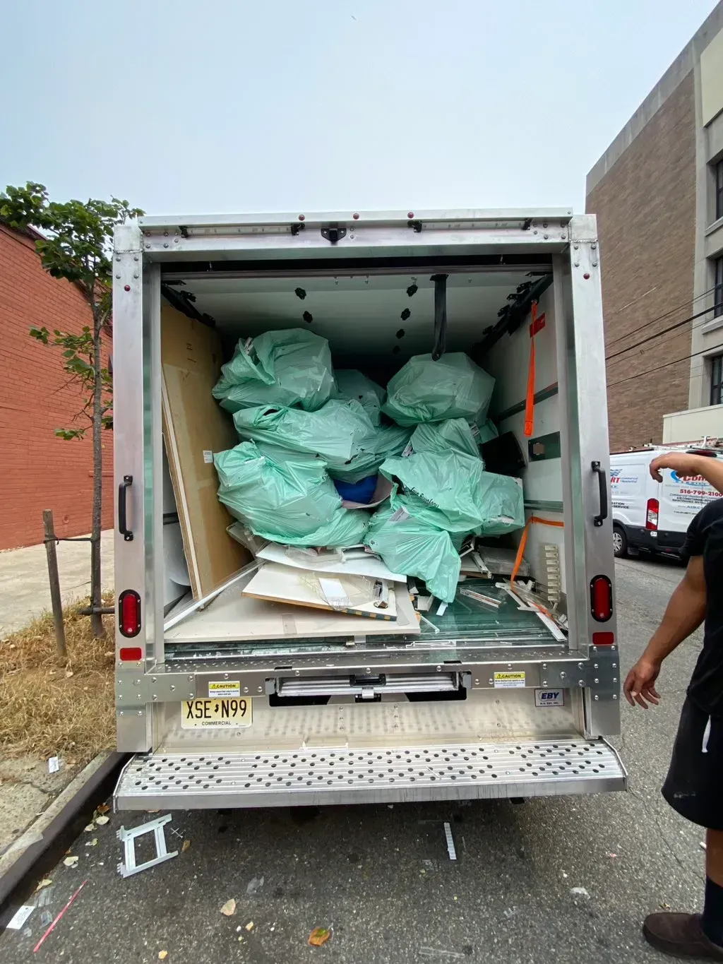 Back of a truck filled with green garbage bags and construction debris on a city street.