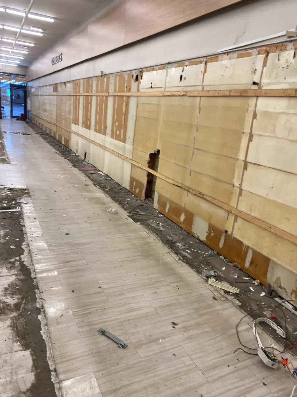 Construction site. Corridor with damaged walls and flooring. Debris and exposed wood visible.