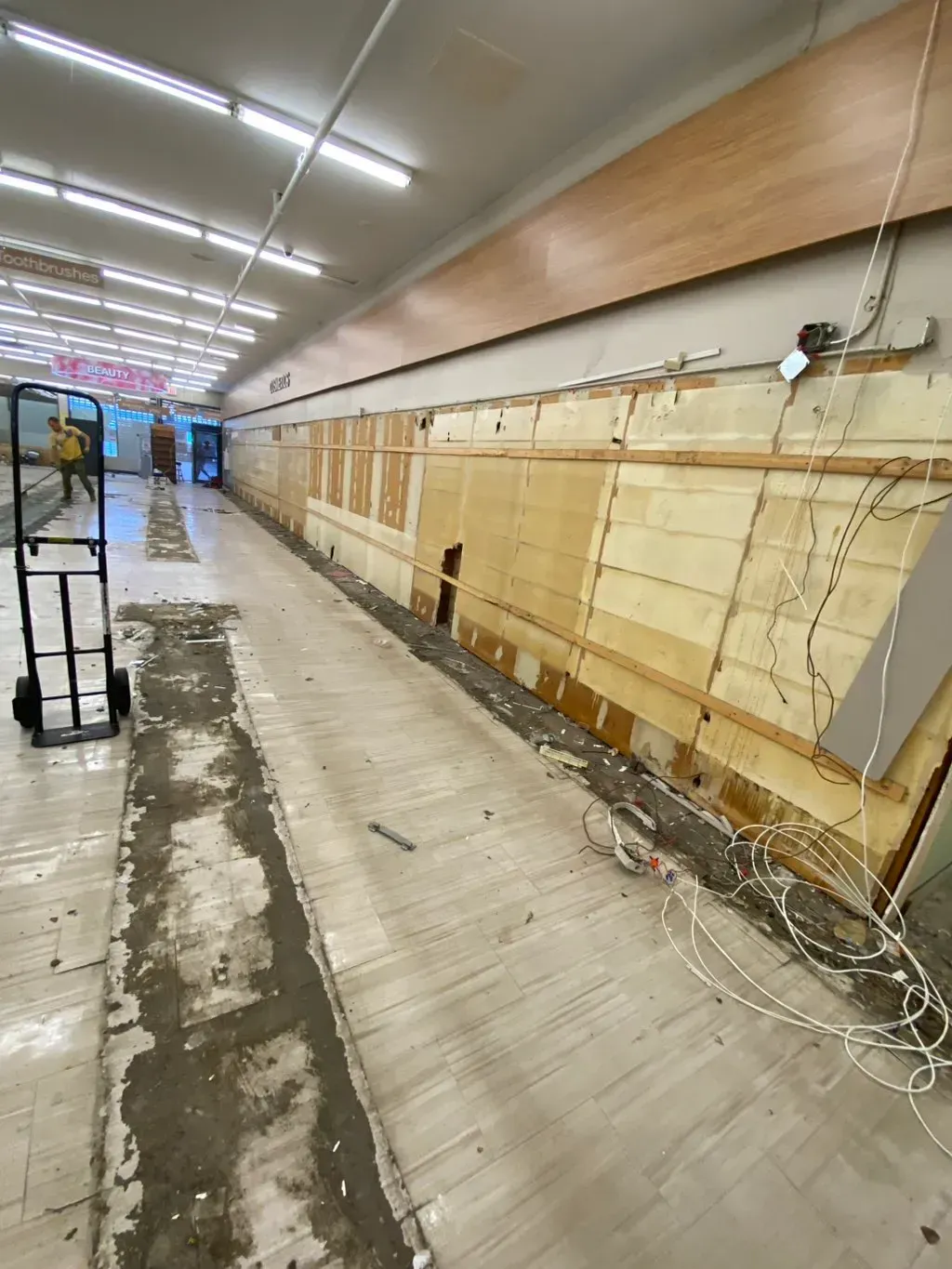 Interior view of a gutted building. A long, narrow hallway with exposed walls and wires; a hand truck is on the left.
