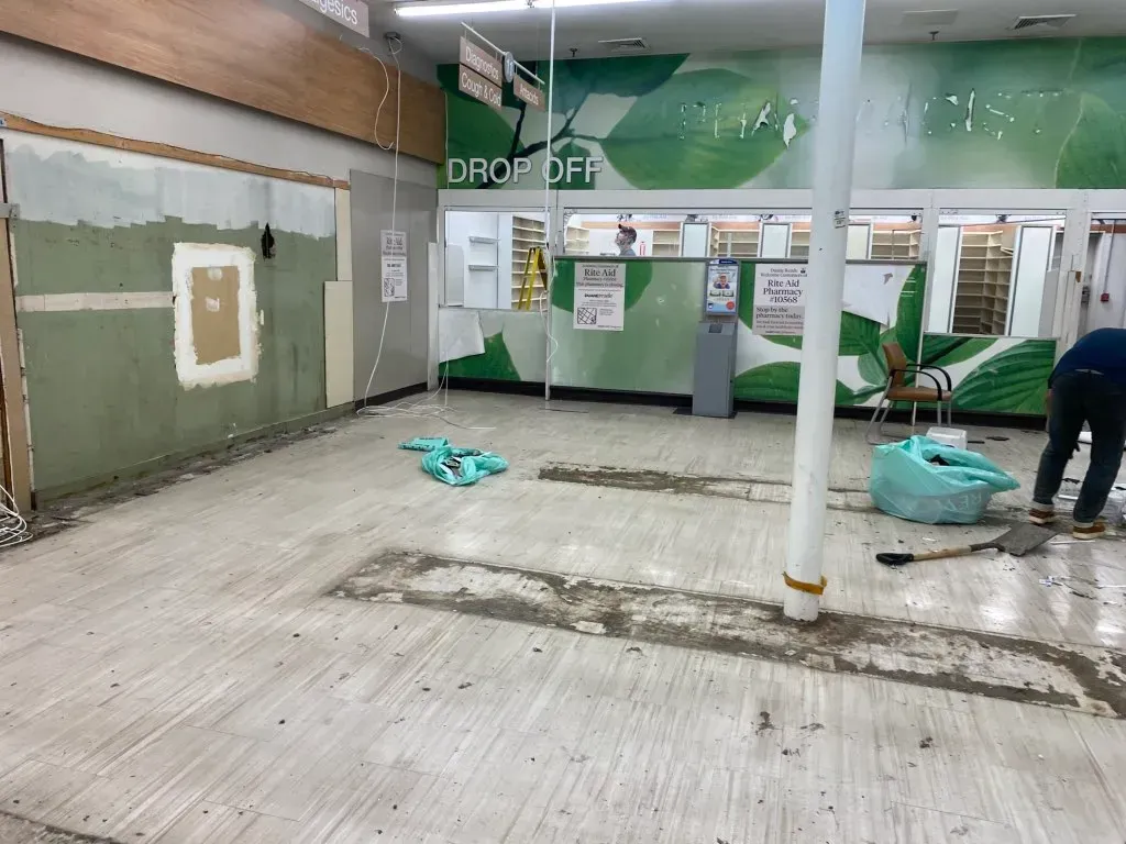 Interior of a store under renovation; walls stripped, debris on floor, person working.