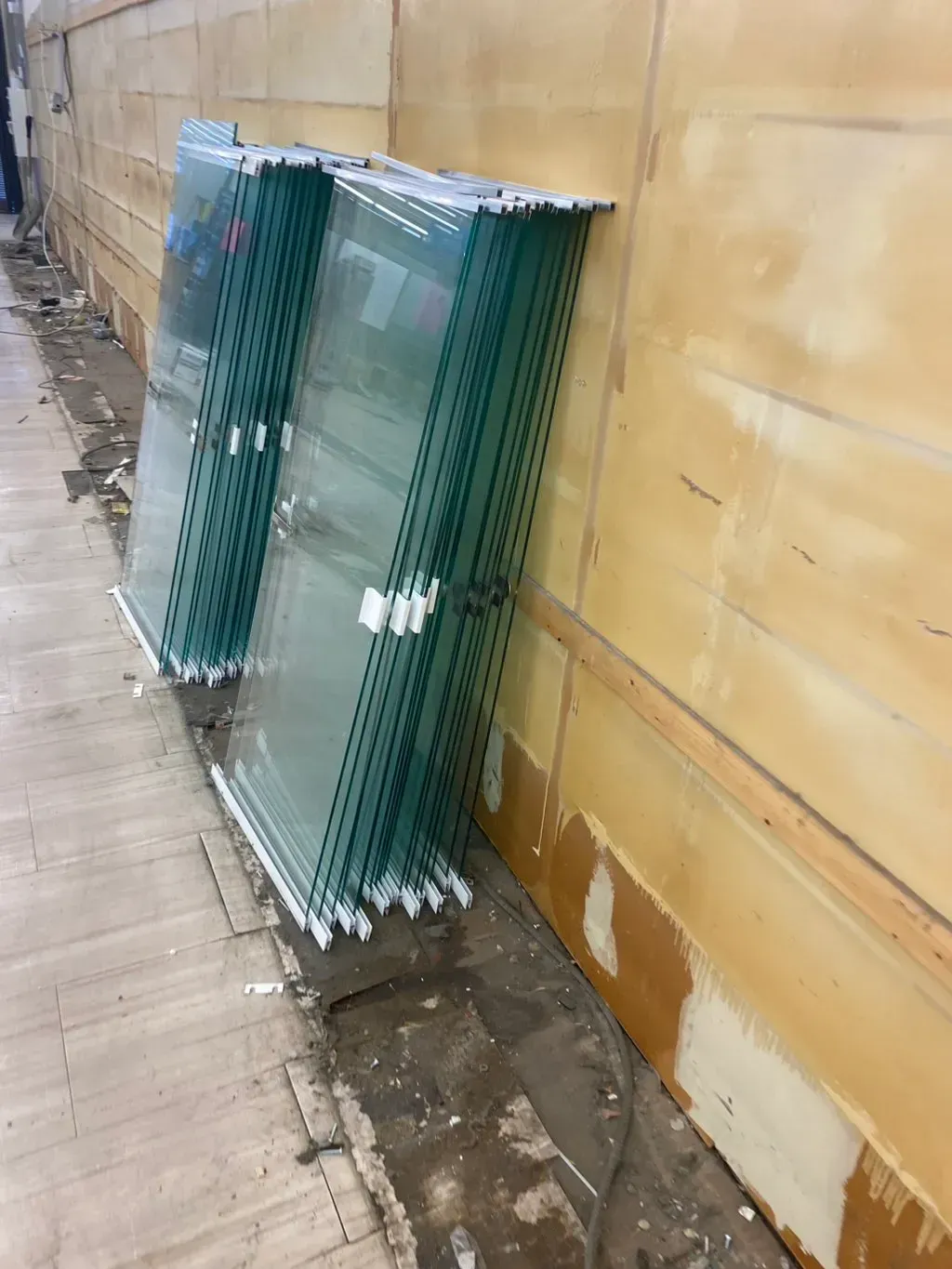 Two stacks of wrapped glass panels leaning against a tan wall in a construction zone.
