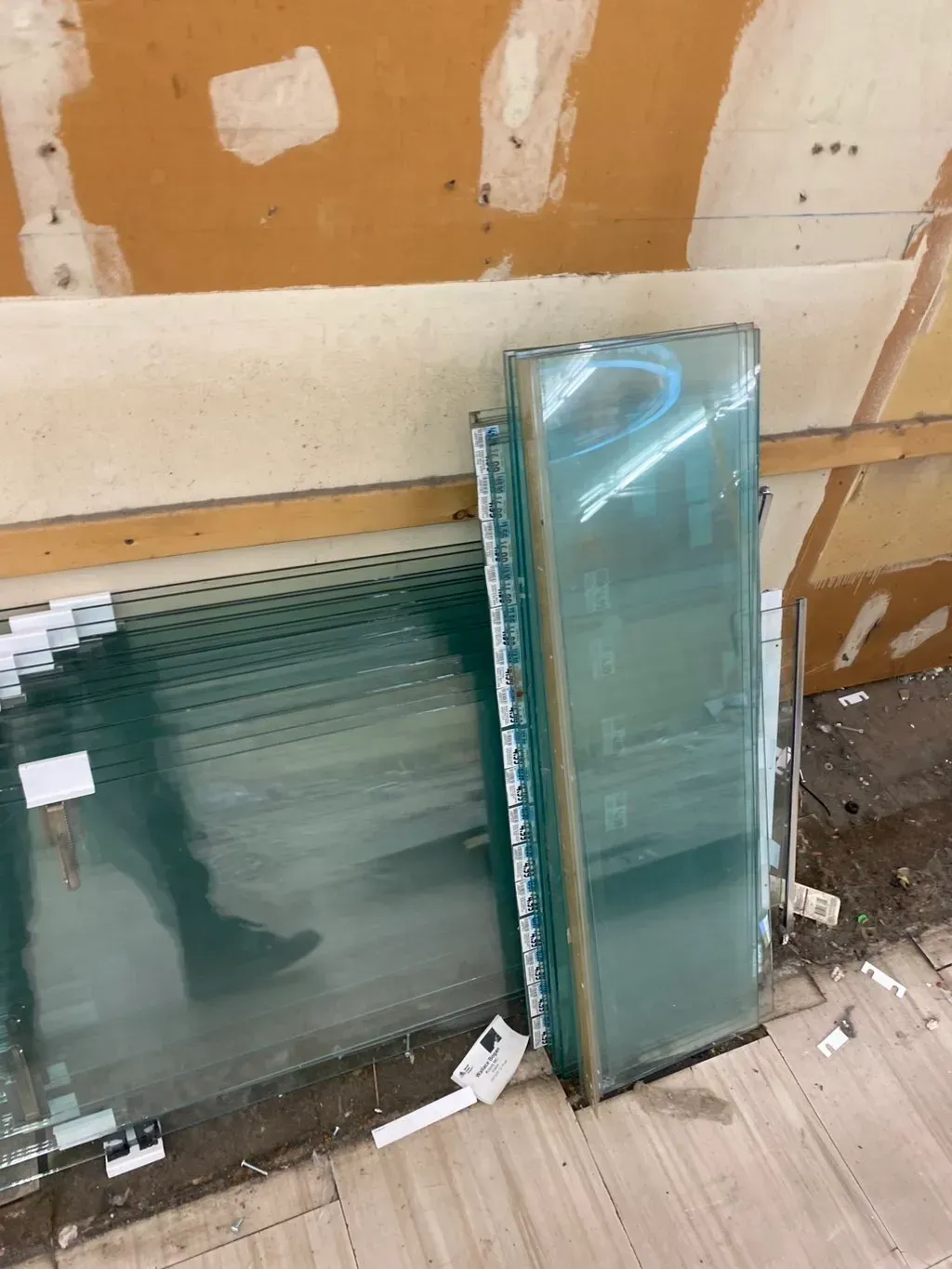 Stack of rectangular glass panels with white trim, leaning against a wall.