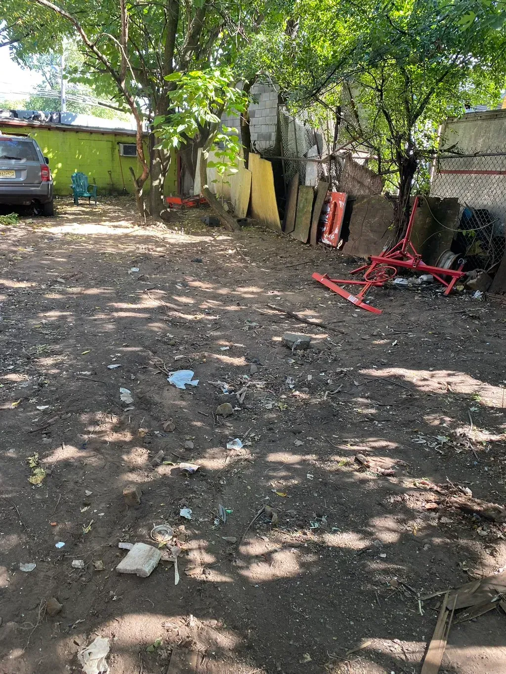 Dirt lot with debris and red metal structures. Green and gray structures in background.