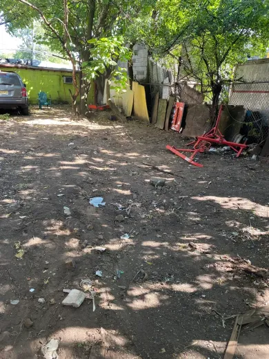 Dirt yard with a car, trees, and various items like plywood and red metal structures.