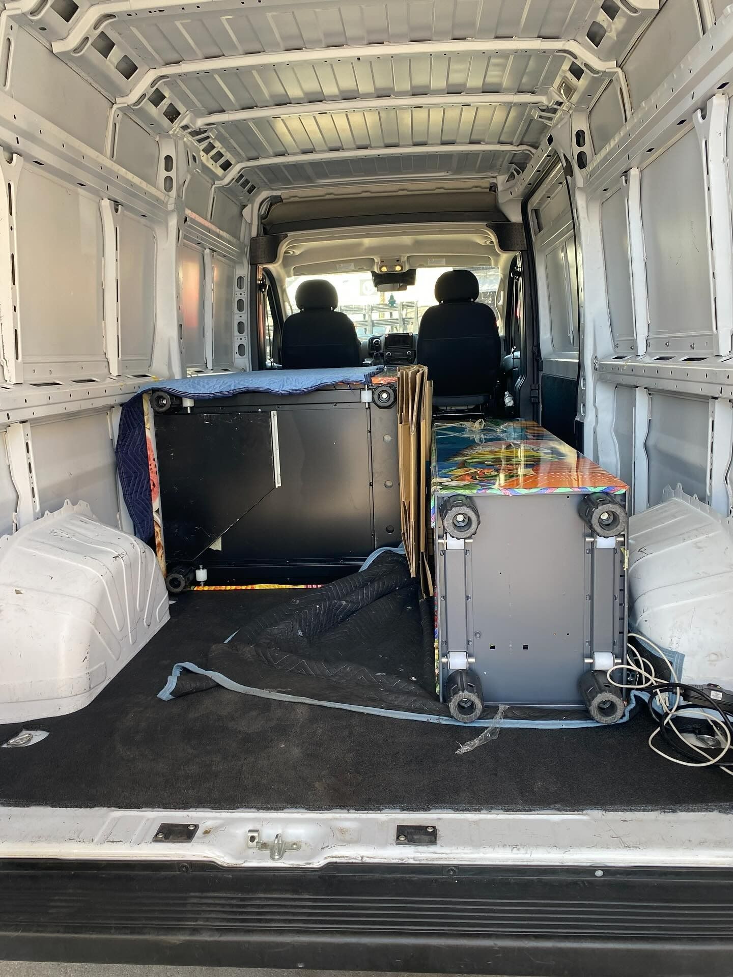 Inside a white cargo van, two large electronic machines are secured for transport.