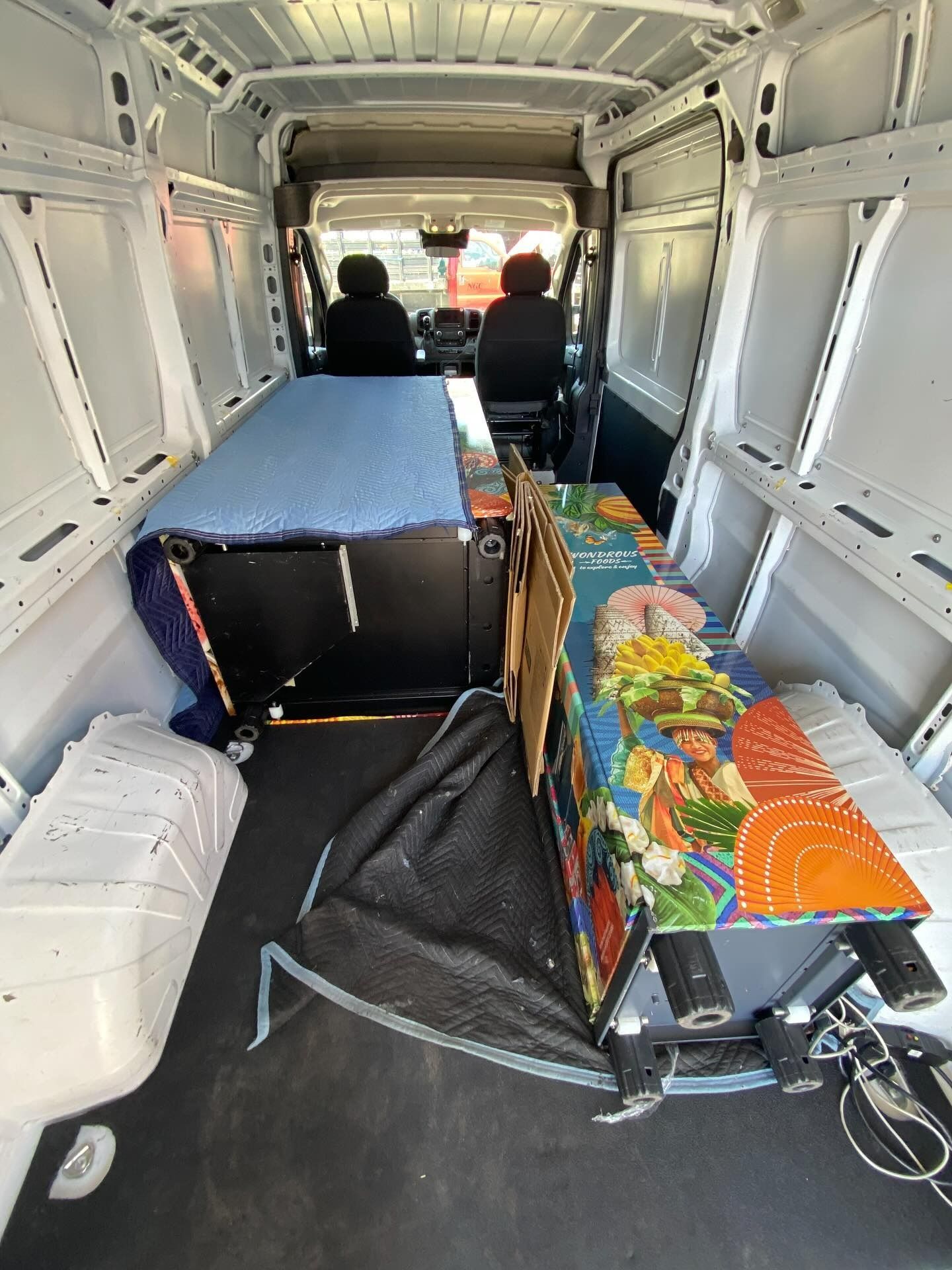 Interior of a van converted for living; bed and storage visible, two figures in the front seats.