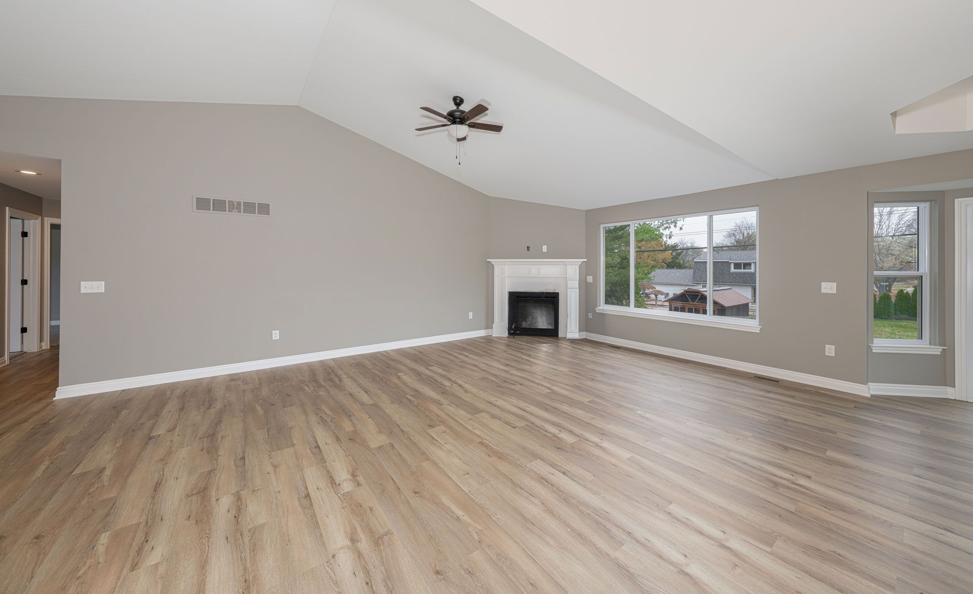 Empty living room with vaulted ceiling, wood floors, fireplace, and large windows.