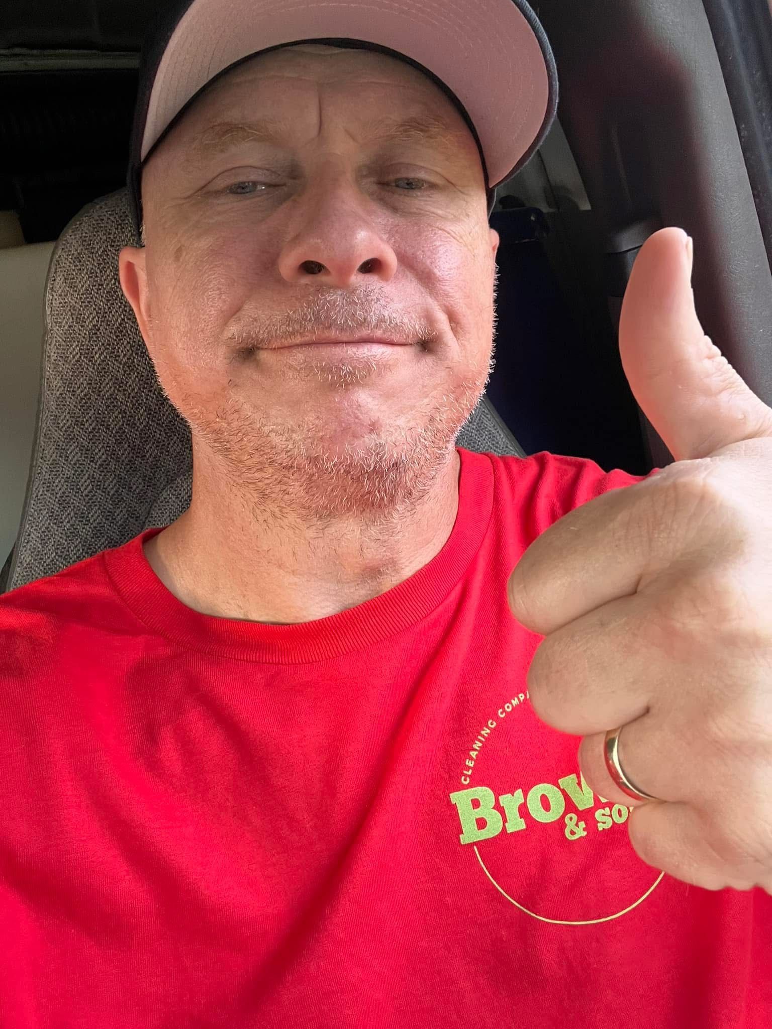 A man in a red shirt and hat is giving a thumbs up.