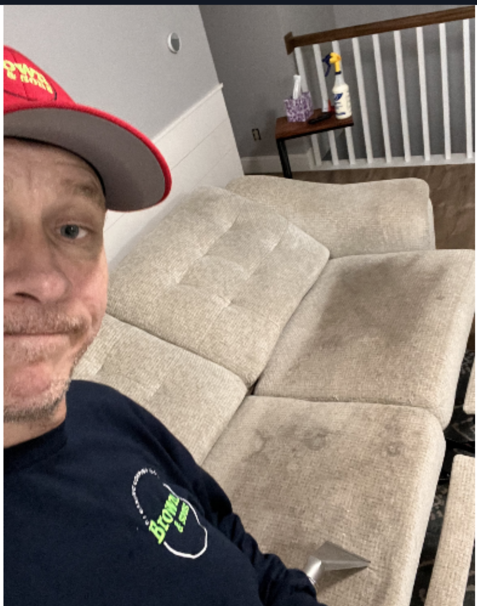A man wearing a red hat is cleaning a couch
