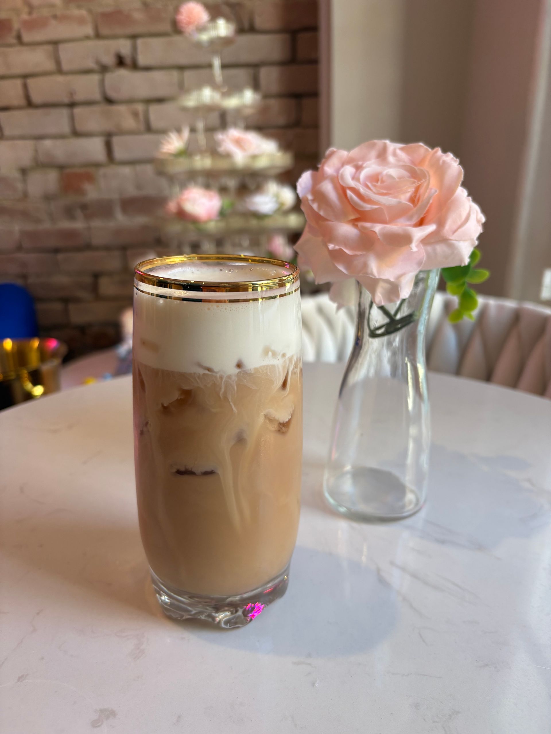 Iced coffee with a creamy top, a pink rose in a vase, and a tower of pink treats.