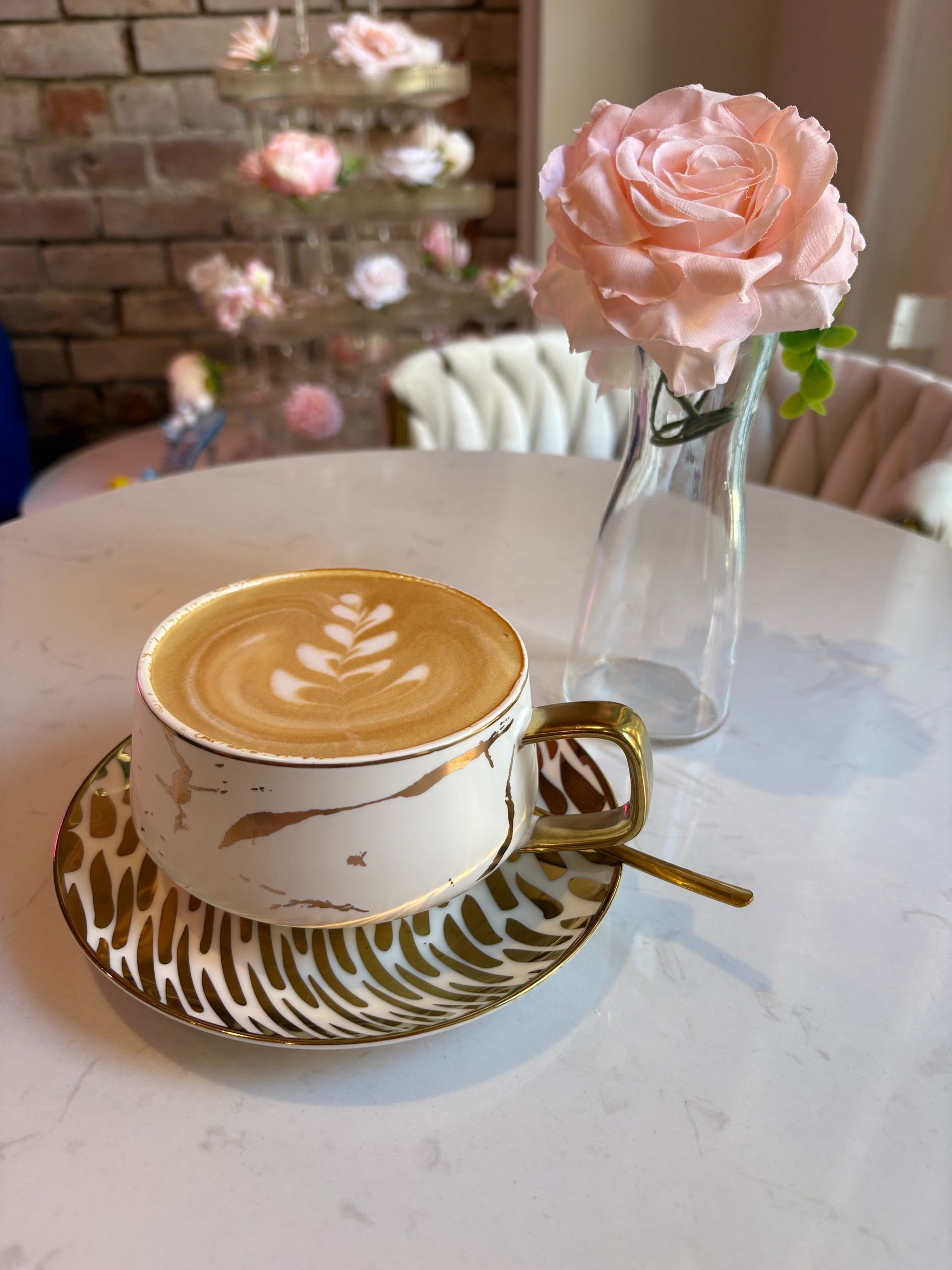 Latte in a decorated cup and saucer, rose in a vase, on a white table.